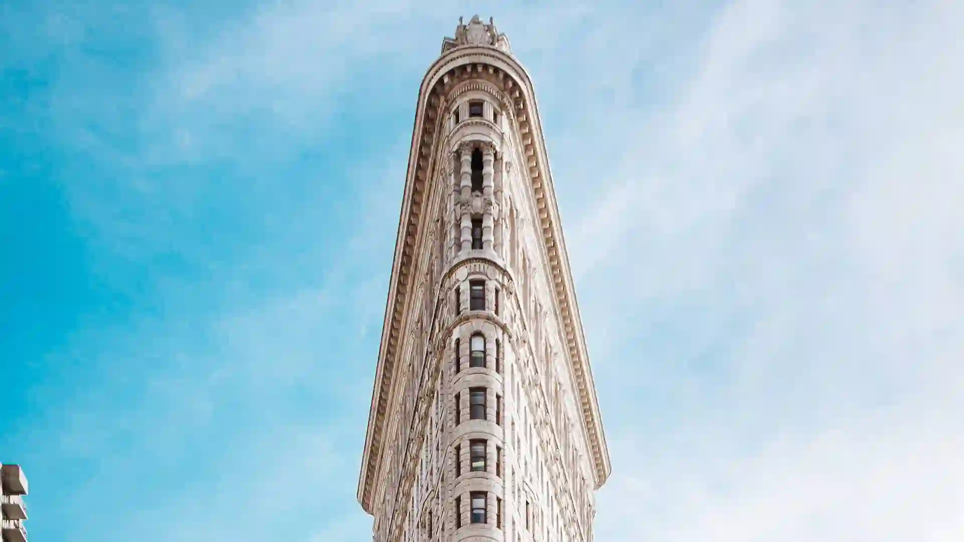 The Flatiron Building is an iconic triangular building located at the intersection of Fifth Avenue and Broadway, known for its unique architecture and historical significance.